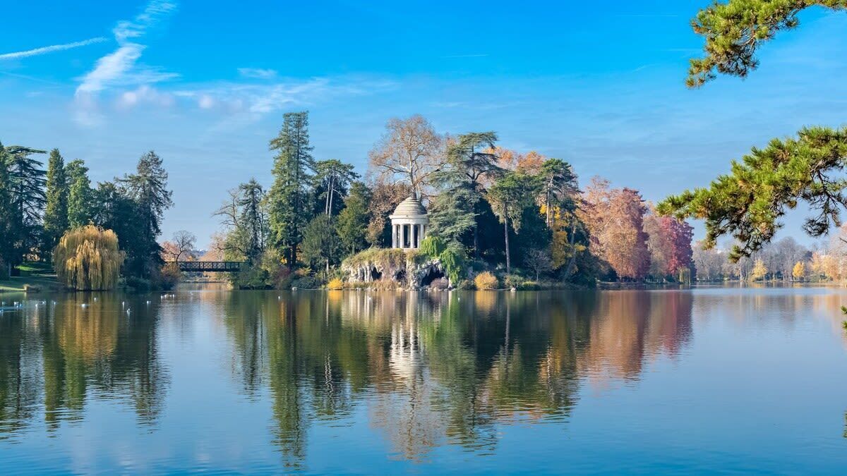 A tranquil lake with a gazebo and trees reflecting on the water.