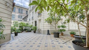 Un patio con suelo de baldosas, plantas en macetas y un edificio con amplias ventanas.