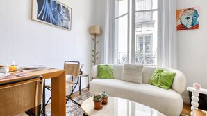 Una sala de estar moderna con un sofá, una mesa de comedor con sillas, una mesa de centro con plantas y obras de arte en las paredes.