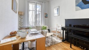 Un comedor con una mesa de madera dispuesta para el desayuno, un piano y un sofá con un cojín verde.