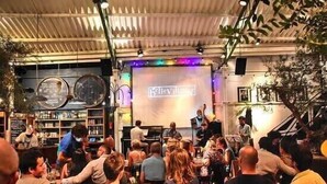 Een drukke bar met een podium en een groot scherm waarop 'Belle Village' staat.
