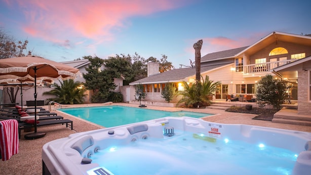 A swimming pool with lounge chairs and a hot tub, surrounded by a house with a balcony and outdoor seating.