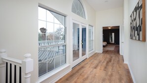 A hallway with wooden flooring, white walls, and large windows.
