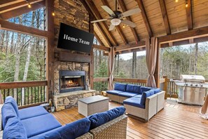 A covered deck with a stone fireplace, outdoor seating, and a grill.