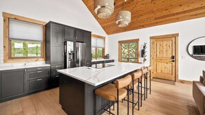 A modern kitchen with a large island, dark cabinets, and wooden ceiling.