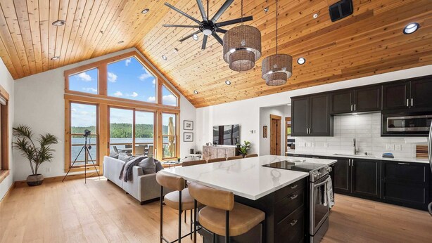 A modern kitchen with a large island, dark cabinets, and a view of the outdoors.