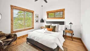 A bedroom with a bed, a ceiling fan, a nightstand, and a window with blinds.