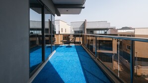 A balcony with a blue floor, glass railings, and a view of neighboring buildings. - 5blu Residence  (Abuja)