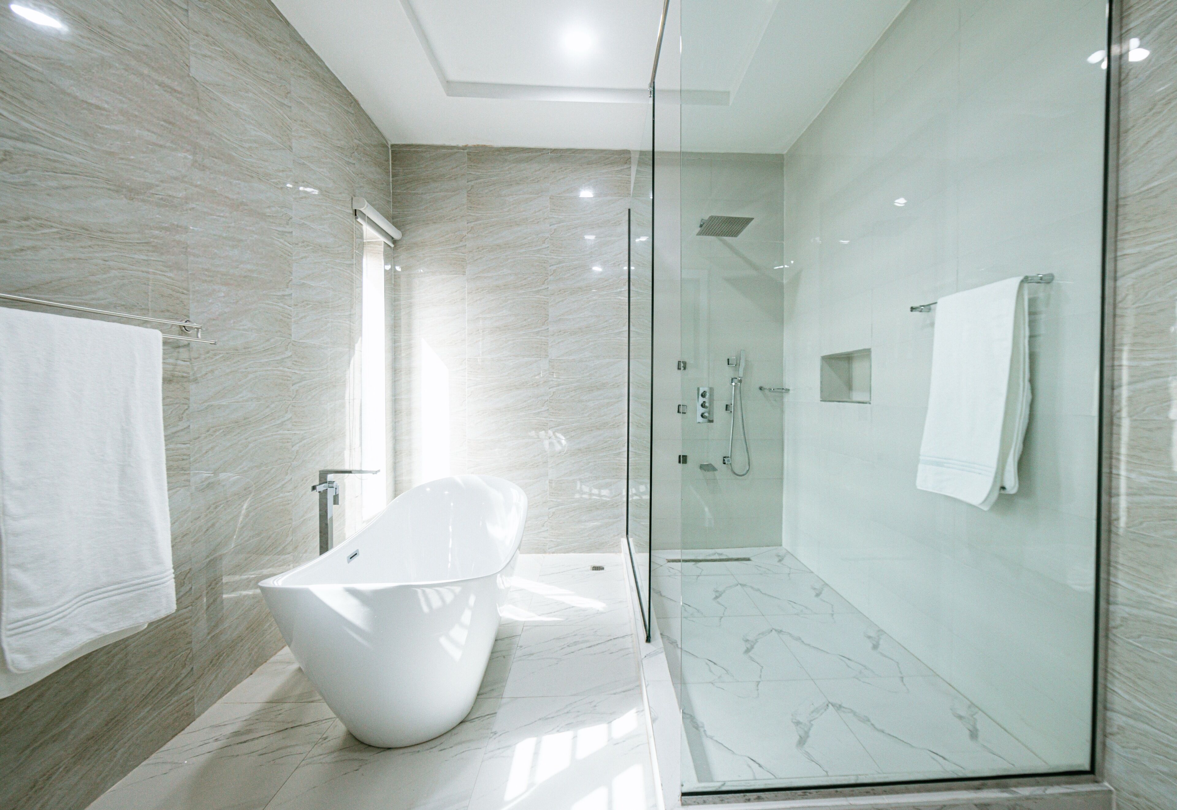A modern bathroom with a freestanding bathtub, a glass-enclosed shower, and marble walls.