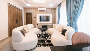A modern living room with a sectional sofa, a flat-screen TV, and a small coffee table. - 5blu Residence  (Abuja)