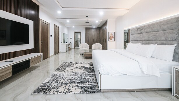 A modern bedroom with a large bed, a TV, and a walk-in closet. - 5blu Residence  (Abuja)