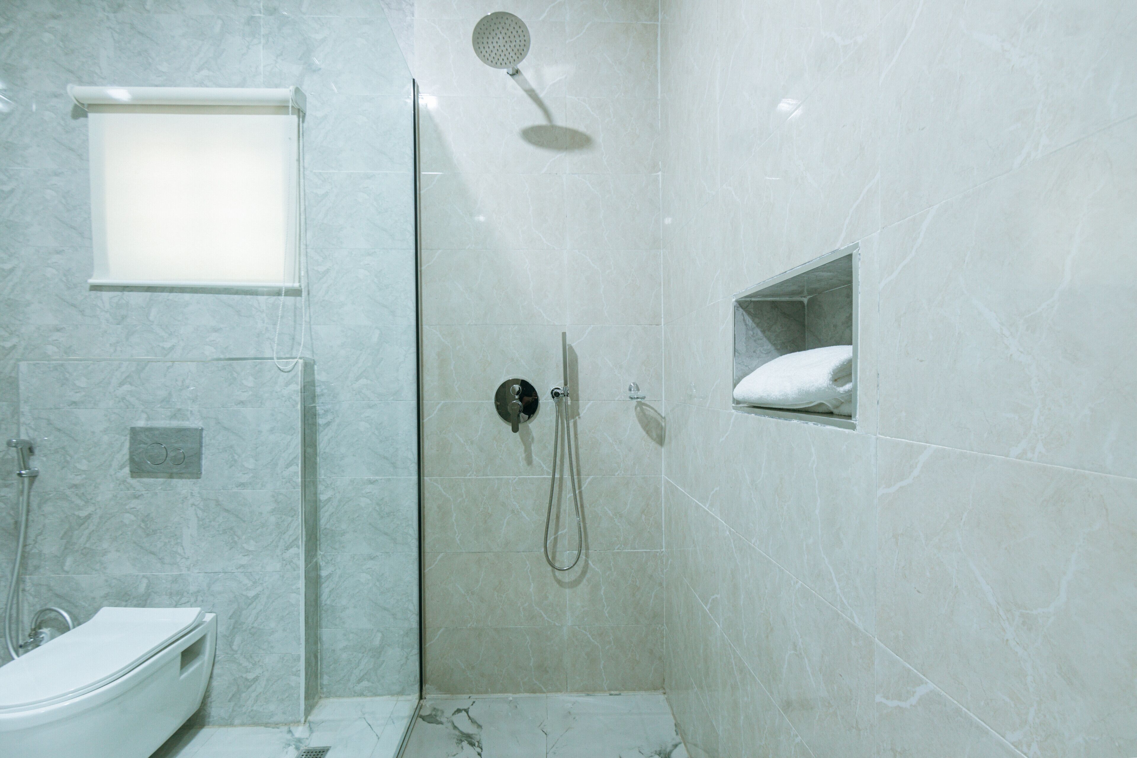 A modern bathroom with a glass-enclosed shower, a toilet, and a small shelf with a towel.