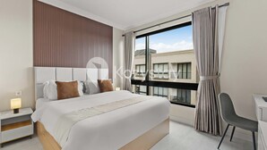 A modern hotel room with a large bed, a desk, and a view of buildings through the window.