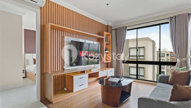 A modern living room with a large flat-screen TV, wooden paneling, a sofa, a coffee table, and a view of the city through large windows.