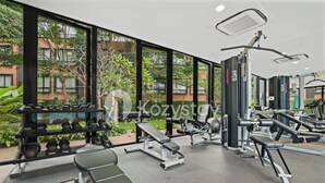 A gym with various exercise equipment, large windows, and a view of greenery and buildings outside.
