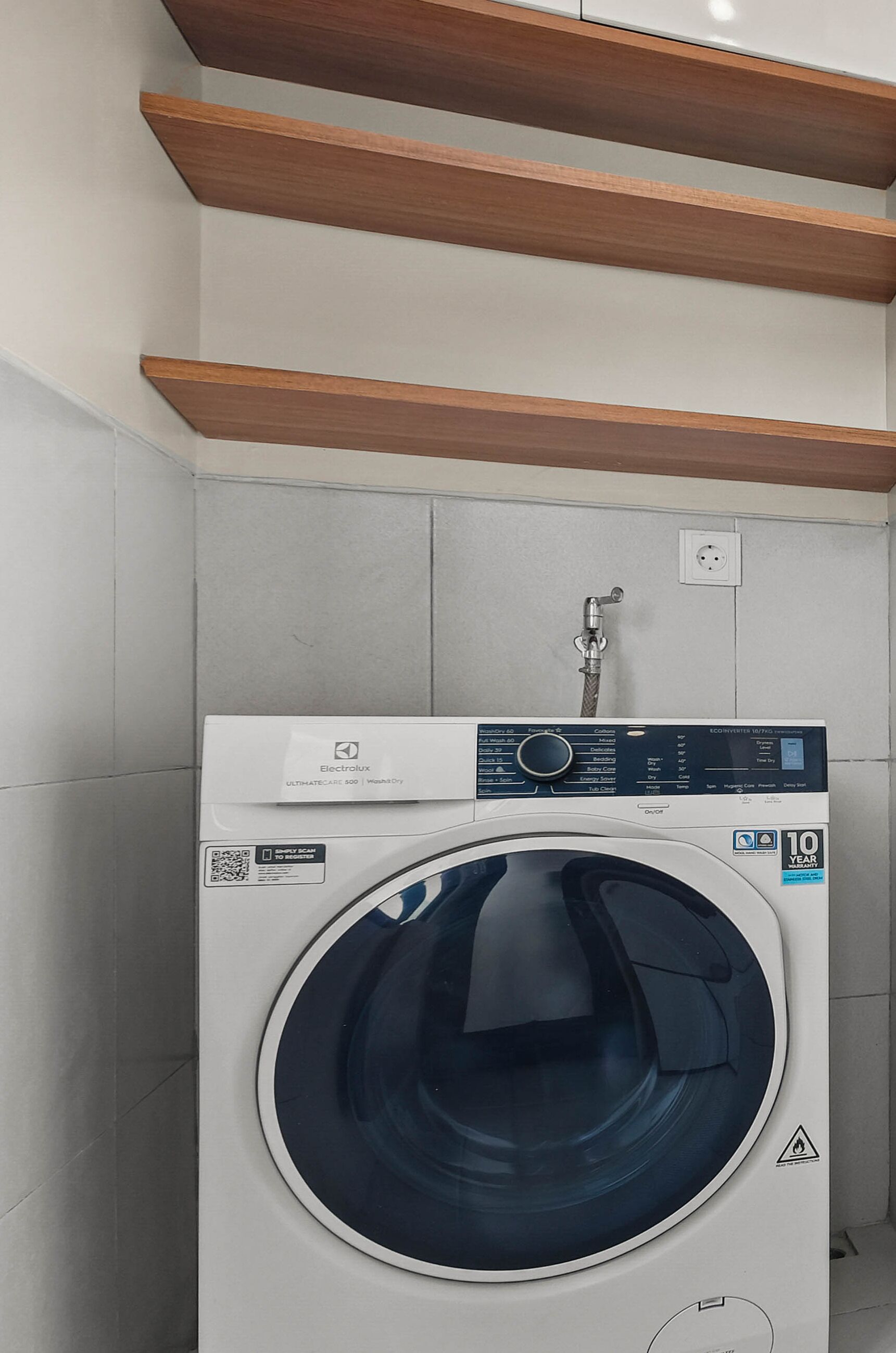 A front-loading washing machine with a control panel, a water inlet hose, and a 10-year warranty sticker.