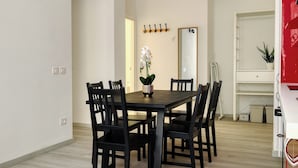 Ein Essbereich mit einem Holztisch und schwarzen Stühlen, einer Vase mit weißen Blumen, einem Kleiderständer und einem Spiegel an der Wand.