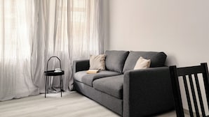 Ein modernes Wohnzimmer mit einem grauen Sofa, einem kleinen schwarzen Beistelltisch und einem weißen Vorhang.