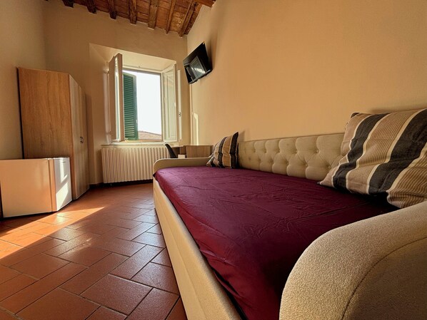 A bedroom with a bed, a television, a radiator, and a window with shutters. - Window To The Tower (Pisa)