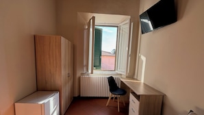 A small room with a wooden wardrobe, a white radiator, a desk with a chair, and a bed. - Window To The Tower (Pisa)