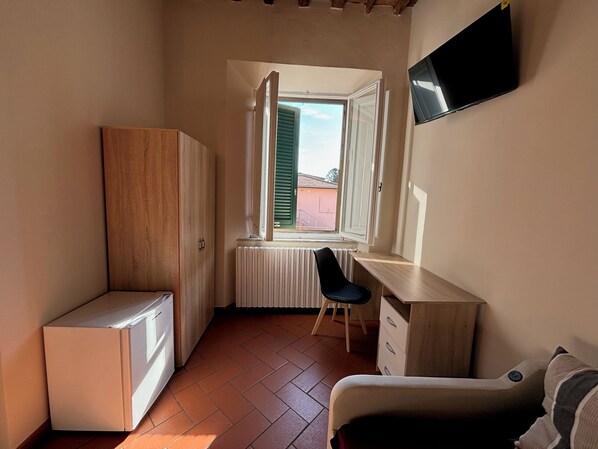 A small room with a wooden wardrobe, a white radiator, a desk with a chair, and a bed.