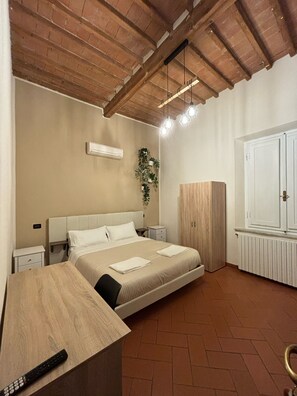 A bedroom with a bed, bedside tables, a wardrobe, and a desk with a remote control. - Window To The Tower (Pisa)