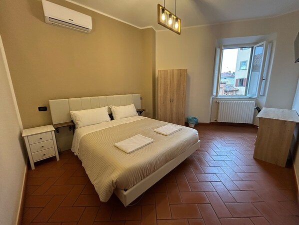 A bedroom with a bed, bedside tables, an air conditioner, a window, and a radiator. - Window To The Tower (Pisa)
