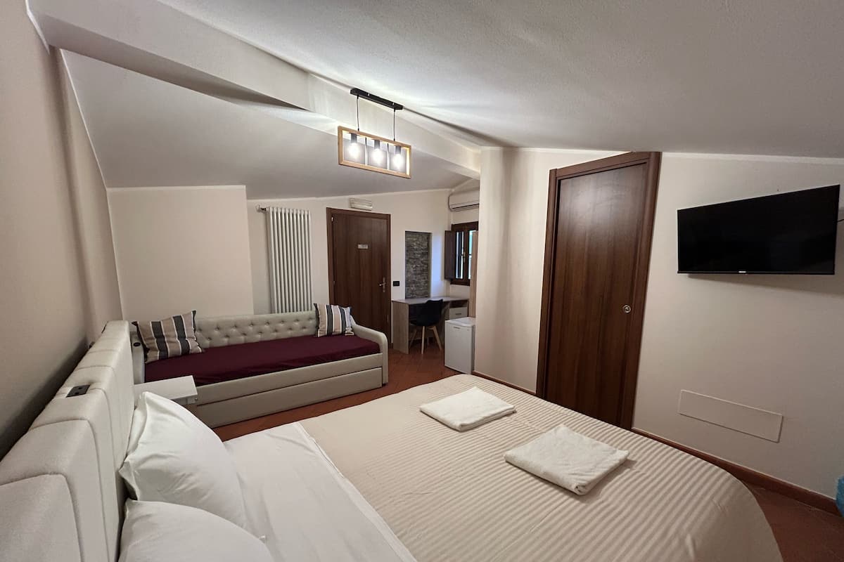 Hotellihuone, jossa on suuri sänky, sohva, työpöytä, televisio ja vaatekaappi.