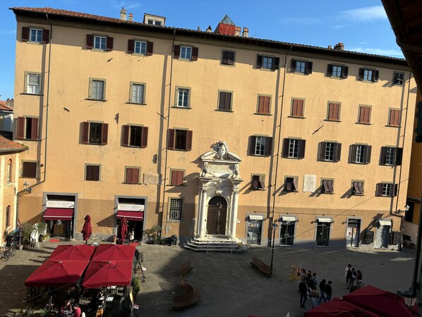 A courtyard with outdoor seating, a fountain, and a building with multiple windows and a statue.