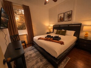 Habitación de hotel con una cama grande, un escritorio, una silla, un televisor y una ventana con cortinas.