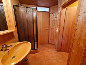 Une salle de bain en bois avec un lavabo, un miroir et une porte donnant sur une zone douche.