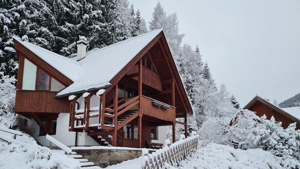A wooden cabin with a balcony, surrounded by snow-covered trees.
