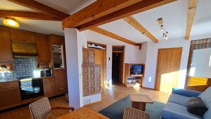A spacious living area with a wooden dining table, a sofa, and a television in the background.