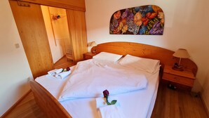 A neatly made bed with white linens, a wooden headboard, and a single rose on the pillow.