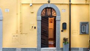 A yellow building with a stone archway entrance, a mailbox, and a small window with a plant. - The Lake View (Castel Gandolfo)