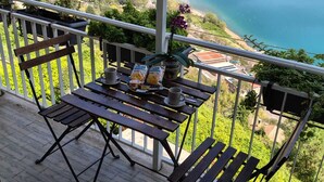 A balcony with a table and chairs overlooking a lake and distant hills. - The Lake View (Castel Gandolfo)