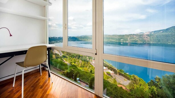 A room with a large window overlooking a lake and hills. - The Lake View (Castel Gandolfo)