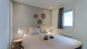 A bedroom with a large bed, two bedside tables, a round side table, and a window with curtains.