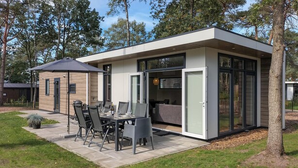 A modern outdoor dining area with a table and chairs, a potted plant, and a glass-enclosed structure with a sliding door.