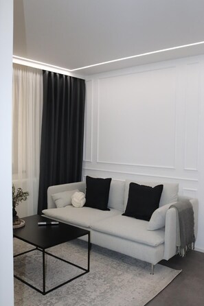 Ein modernes Wohnzimmer mit einem hellen Sofa, schwarzen Kissen, einem schwarzen Couchtisch und einem gemusterten Teppich.