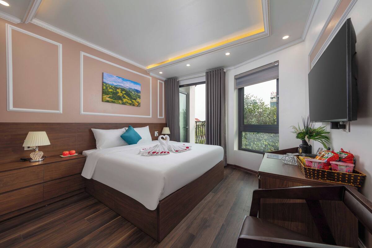 Une chambre d’hôtel avec un grand lit, un bureau avec une chaise, une télévision et une fenêtre avec des rideaux.