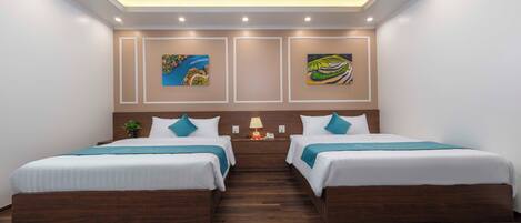 A hotel room with two beds, wooden flooring, a ceiling with recessed lighting, and artwork on the walls.