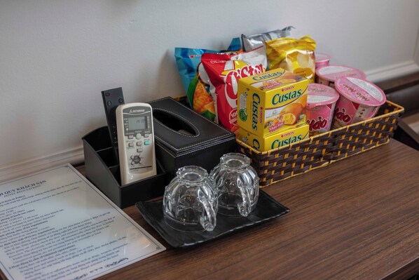 Een hotel receptiebalie met een telefoon, een zwarte dienblad met twee glazen, een mand met snacks, waaronder Custus en andere verpakte producten, en een menukaart aan de linkerkant.