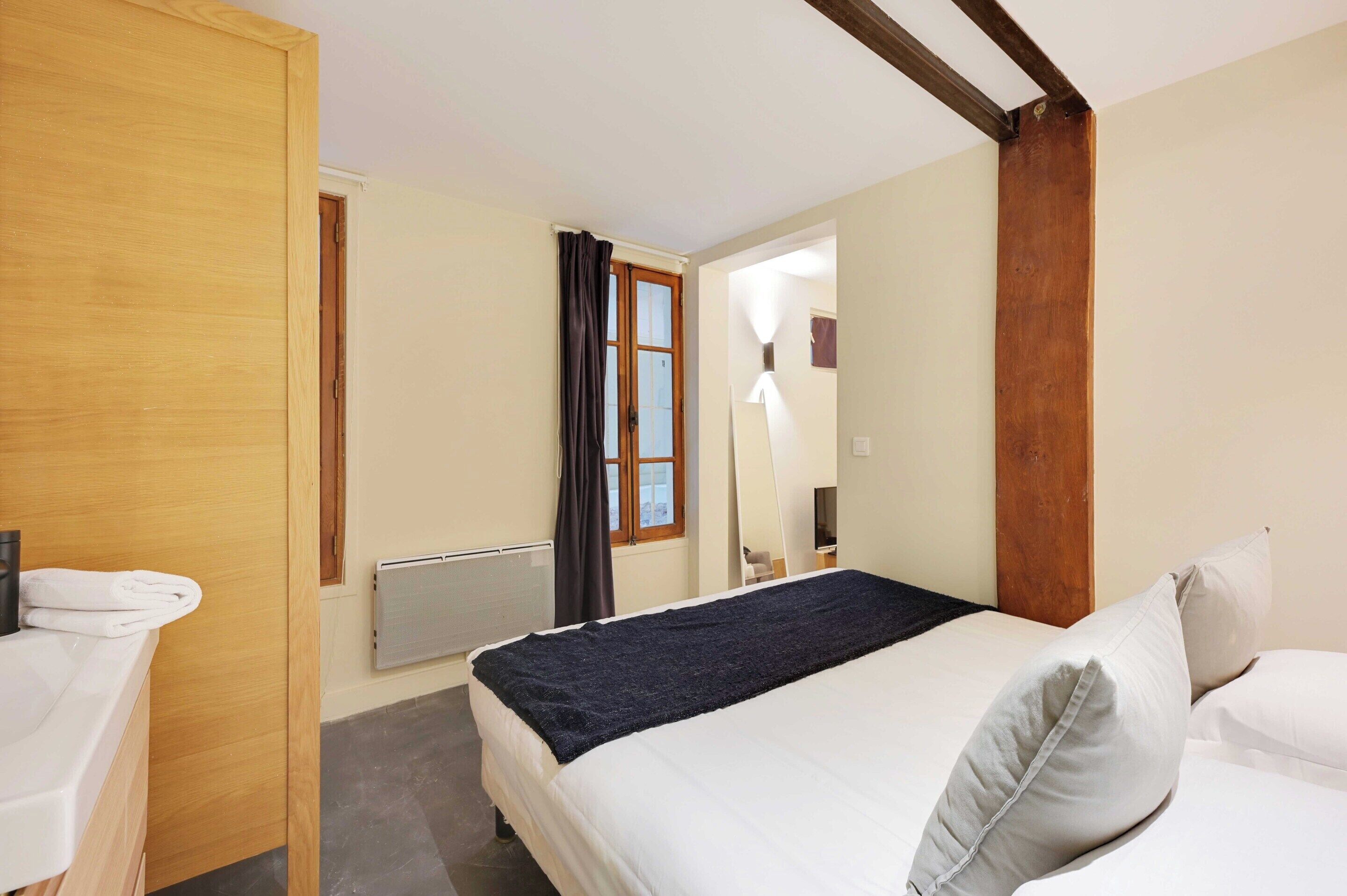 Habitaci ón de hotel con cama, armario de madera, baño con lavabo blanco y ventana con cortinas.
