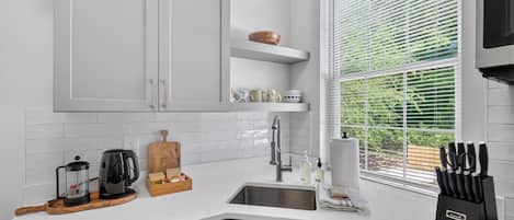 A modern kitchen with white cabinetry, a built-in sink, and a window with blinds.