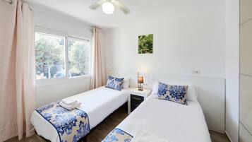A hotel room with two beds, a window with curtains, a ceiling fan, and a wall-mounted lamp.