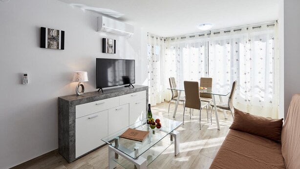A modern living room with a flat-screen TV, a glass coffee table, a sofa, and a dining area with chairs. - Deluxe Apartment, 3 min from the beach (Benidorm)