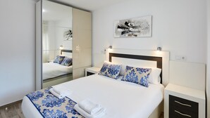 A modern hotel room with a large bed, a bedside table, a nightstand, a mirror, and a wall-mounted artwork. - Deluxe Apartment, 3 min from the beach (Benidorm)