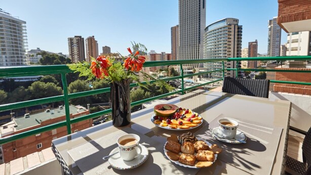 A balcony with a table set for a meal, a vase with flowers, and a cityscape view. - Superior Apartment with Balcony and Sea View (Benidorm)