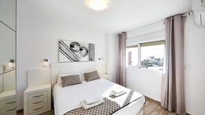 A modern bedroom with a large bed, bedside tables, a wall-mounted artwork, and a window with curtains. - Superior Apartment with Balcony and Sea View (Benidorm)